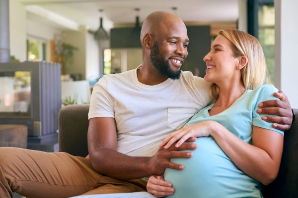 Loving couple with pregnant woman on sofa at home
